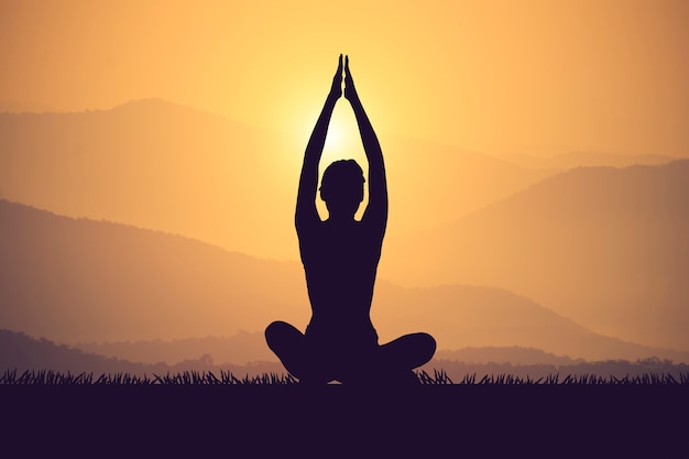 Übendes Yoga der jungen Frau des Schattenbildes auf dem muontain bei Sonnenuntergang Weinlesefarbe