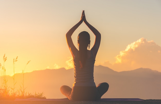 Übendes Yoga des Silhouettieren Sie Eignungsmädchens auf Berg mit Sonnenlicht