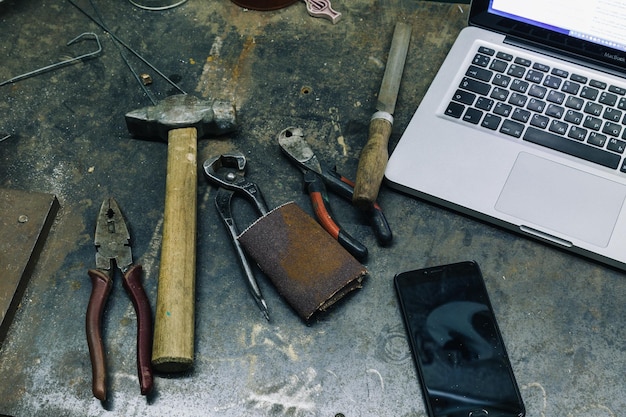 Foto Über ansicht von gebrauchten hammerzangen und meißeln mit laptop und smartphone auf metalltisch