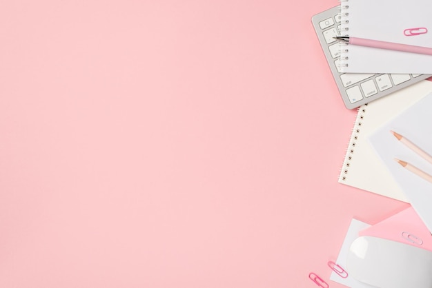 Über dem Foto der Tastatur viele Notizbücher, Stifte, Büroklammern und Computermaus isoliert auf dem rosa Hintergrund mit Leerzeichen