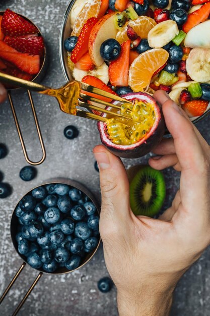 Foto Überblick über frische früchte auf dem tisch mit passionsfrucht in der hand, die gegessen wird