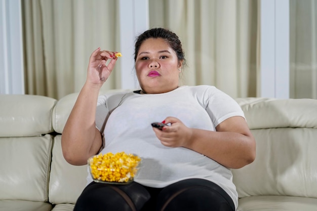 Foto Übergewichtige frau isst popcorn und schaut auf dem sofa fern