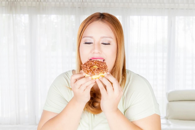 Übergewichtige Frau isst zu Hause Donuts