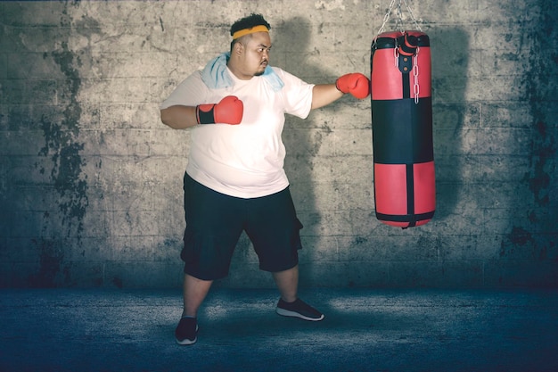 Foto Übergewichtiger mann schlägt einen boxsack gegen die wand