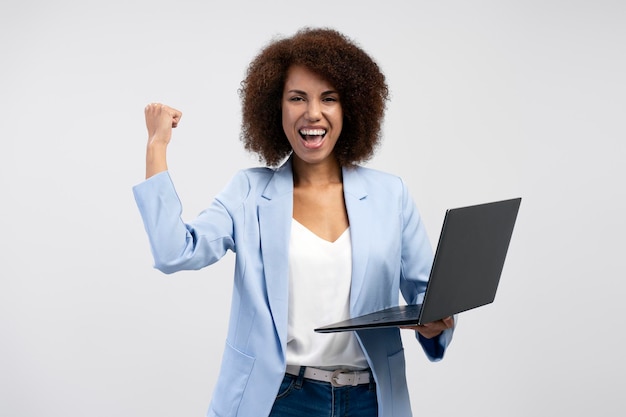 Überglückliche Afroamerikanerin, die den Erfolg der Laptop-Computerfeier isoliert auf dem Hintergrund hält