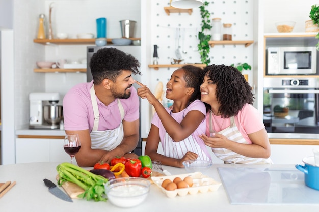 Überglückliche junge Familie mit Tochter hat Spaß beim Backen von Gebäck oder Kuchen zu Hause zusammen. Glücklich lächelnde Eltern genießen das Wochenendspiel mit dem Kind, das in der Küche Bäckerei kocht