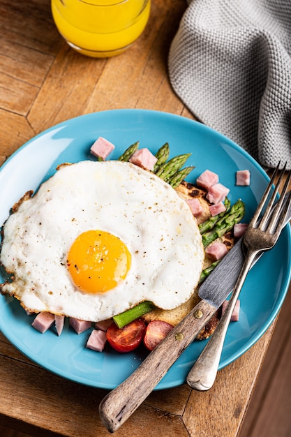 Foto Überkopfaufnahme des frühstücks oder des mittagessens mit spiegelei, brottoast, grünem spargel, tomaten und speck auf blauem teller