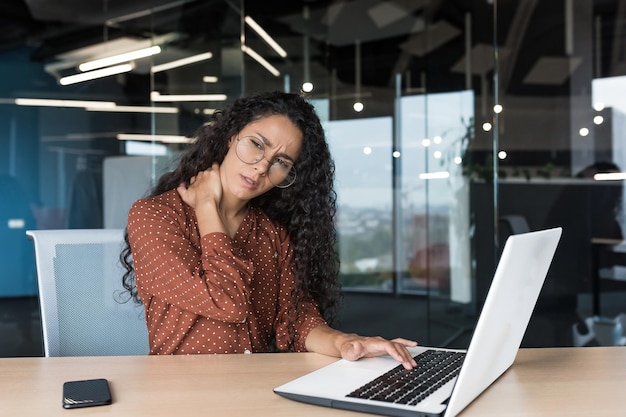 Übermüdete hispanische frau, die in einem modernen büro mit laptop arbeitet geschäftsfrau im bürogebäude