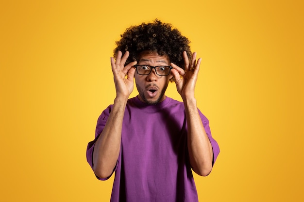 Foto Überraschen sie erwachsenen afroamerikanischen lockigen mann in lila t-shirt mit offenem mund nimmt brille ab