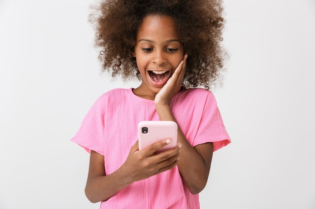 überrascht schockiert junges afrikanisches Mädchen Kind posiert isoliert über weiße Wand, mit Handy.