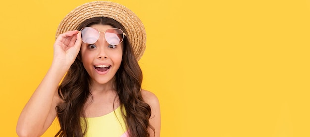 Foto Überrascht teenager-mädchen in strohhut und brille hat lockiges haar auf gelbem hintergrund einkaufsverkäufe kindergesicht horizontales poster teenager-mädchen isoliertes porträtbanner mit kopierbereich