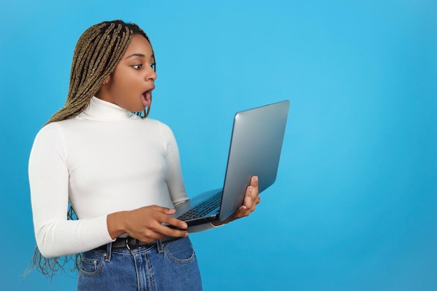 Überraschte afrikanische Frau, die einen Laptop hält