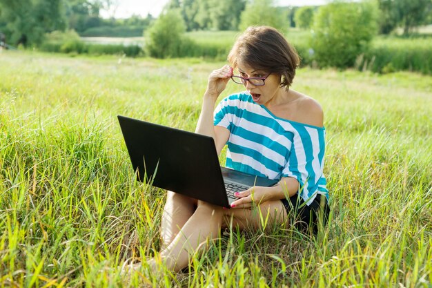 Überraschte frau schaut auf laptop-monitor frau freiberuflich, in der natur arbeiten