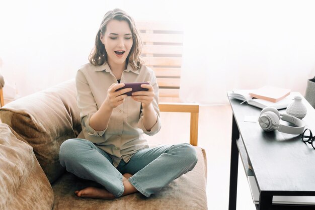 Foto Überraschte millennial reaktion fröhliche frau mit offenem mund schaut auf das telefon liest nachricht spielt m