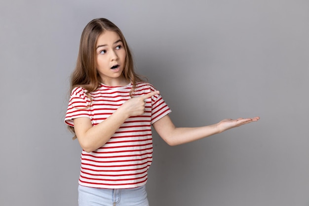 Überraschtes kleines Mädchen, das auf einen leeren Platz auf ihrer Handfläche zeigt, um Ideen zu präsentieren