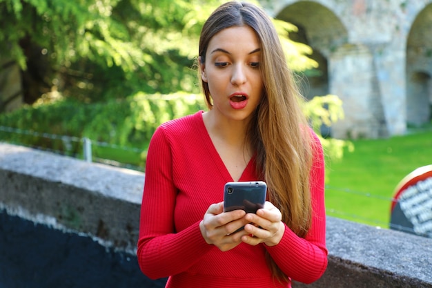 Überraschtes Mädchen, das gute Nachrichten am Smartphone sucht