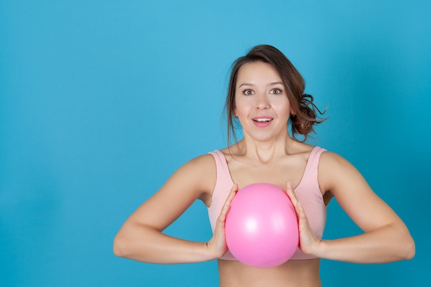 überraschtes Mädchen in einem rosa Sportoberteil, das einen Pilatesball umklammert