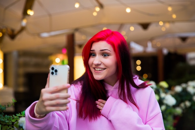 Überraschtes rothaariges Influencer-Blogger-Mädchen, das über das Smartphone mit ihren Abonnenten in sozialen Netzwerken Videoanrufe macht.