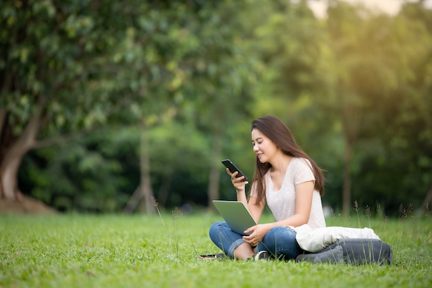 Überzeugte lächelnde recht junge frau, die auf arbeitsplatz in im freien mit laptop sitzt. arbeitskonzept