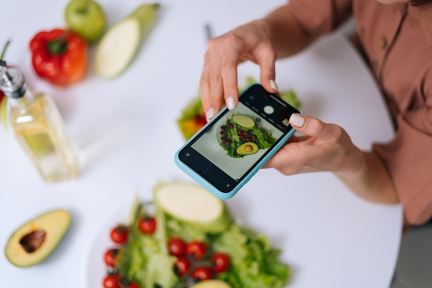 UFA RUSIA 18 DE MARZO DE 2020 Vista de cerca de una mujer haciendo fotos de ensalada de verduras con una cámara de teléfono celular para colocar fotos en los recursos de las redes sociales Concepto de alimentación saludable