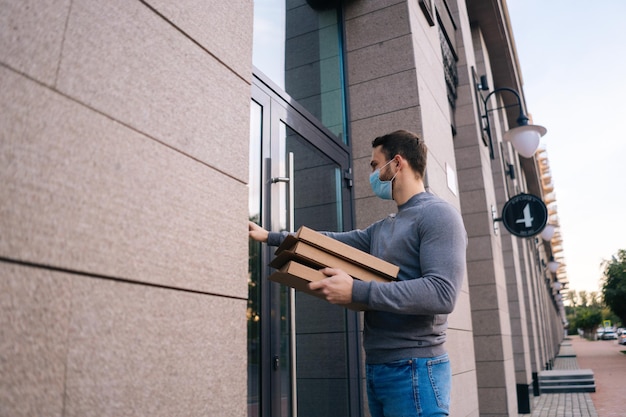 Ufa, rússia - 13 de setembro de 2020 entregador usando máscara médica porta de toque para caixas de papelão de entrega com pizza quente entregador em máscara protetora segurando caixa com comida.