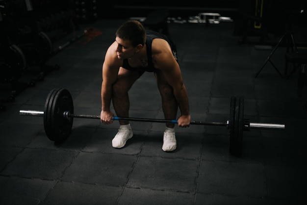 UFA RUSSLAND 31. OKTOBER 2019 Muskulöser junger Mann mit perfektem, schönem Körper in Sportbekleidung, der während des Sporttrainings in einem modernen dunklen Fitnessstudio schwere Hanteln vom Boden hebt