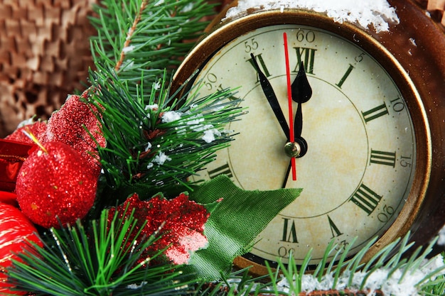 Uhr mit Tannenzweigen und Weihnachtsdekoration auf braunem Hintergrund
