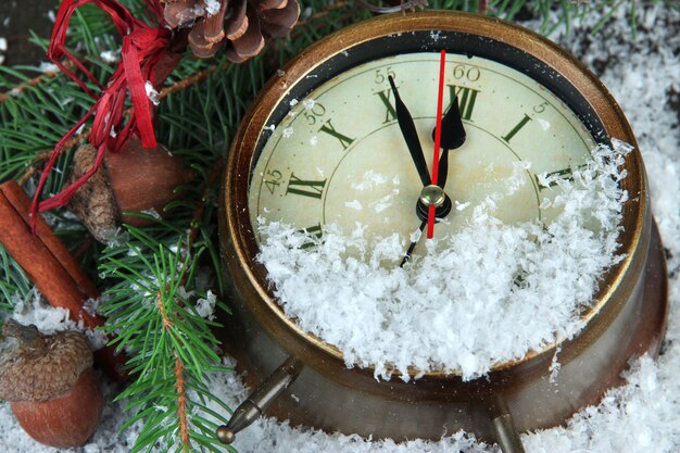 Uhr mit Tannenzweigen und Weihnachtsschmuck unter Schnee hautnah