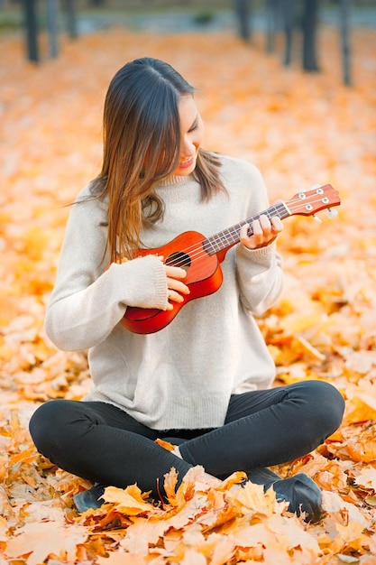 Ukelele en manos de mujer closeup tocando un instrumento acústico ukelele en otoño al aire libre