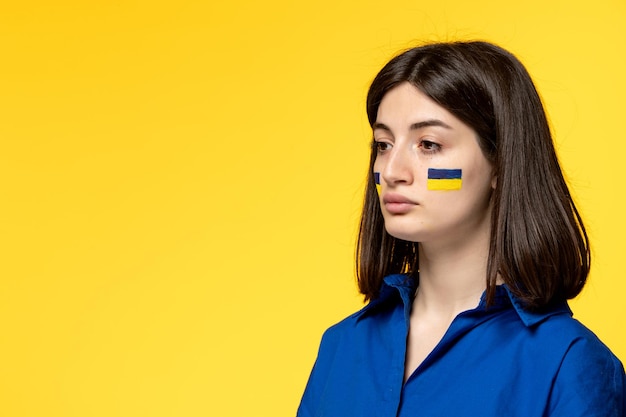 Ukraine russischer Konflikt junges hübsches Mädchen Flaggen auf Wangen gelben Hintergrund Nahaufnahme verärgert