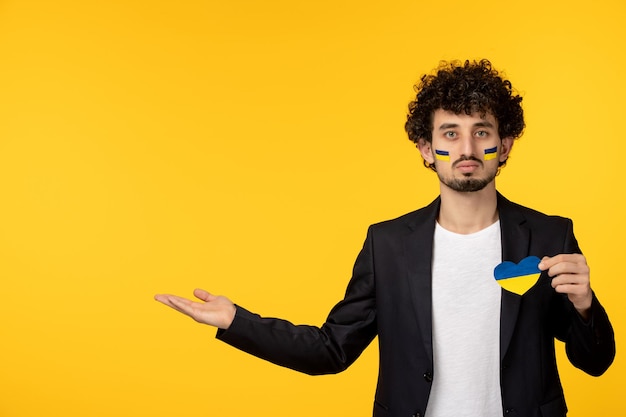 Ukraine-Russland-Konflikt junger Mann im Blazer bemalte ukrainische Flagge auf dem Gesicht mit ukrainischem Herz