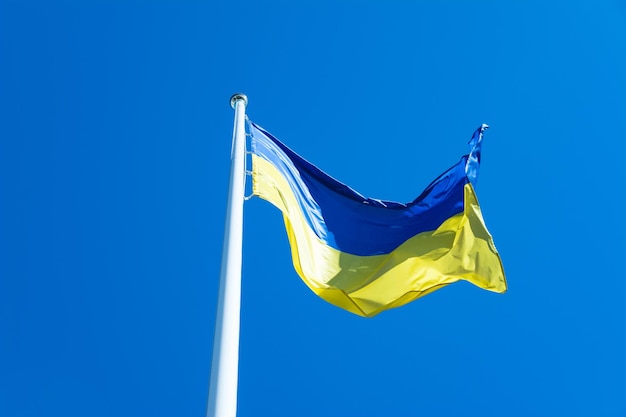 Ukrainische Flagge am Fahnenmast weht im Wind vor blauem Himmelshintergrund.