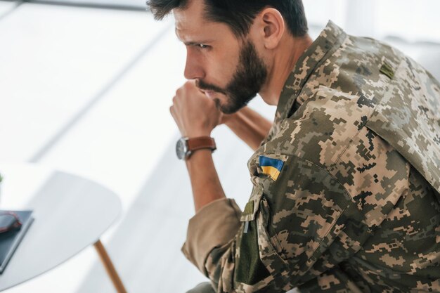 Ukrainische Flagge Soldat in Uniform ist drinnen im Wohnraum