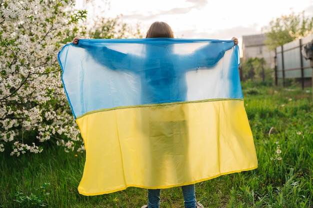 Ukrainische Flagge und Kindersilhouette Silhouette eines Kindes hinter einer ukrainischen Flagge, die von der Nachmittagssonne in einem blau-gelben Porträt beleuchtet wird