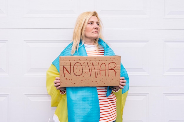 Foto ukrainische frau mit blonden haaren und einer ernsten geste mit einer blau-gelben ukrainischen flagge mit einem schild mit der aufschrift 39no war39 auf der straße konzept ukraine krieg invasion protest patriotismus