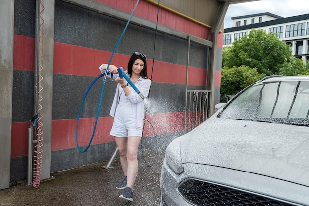 Ukrainische Frau mit Schaumwasserpistole reinigt ihr Auto im Dienst. Reinigungskonzept