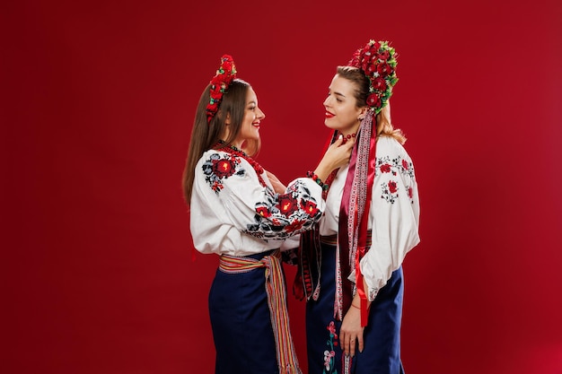 Ukrainische Frauen in traditioneller ethnischer Kleidung und rotem Blumenkranz auf viva magenta Studiohintergrund National besticktes Kleid rufen Vyshyvanka an Beten Sie für die Ukraine