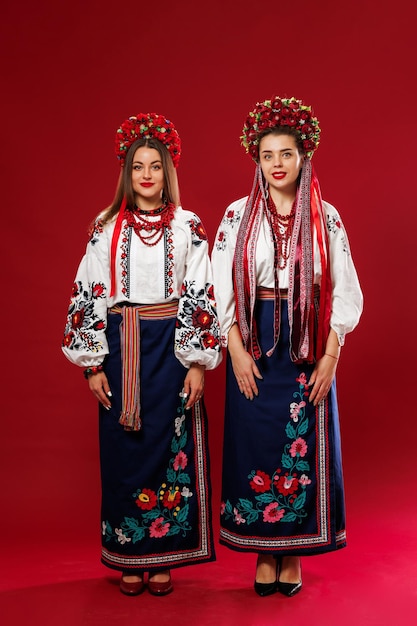 Ukrainische Frauen in traditioneller ethnischer Kleidung und rotem Blumenkranz auf viva magenta Studiohintergrund National besticktes Kleid rufen Vyshyvanka an Beten Sie für die Ukraine