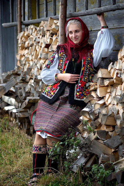 Ukrainische Hutsul-Frau in authentischer Nationaltracht, die in der Nähe einer Holzwand mit Brennholz steht