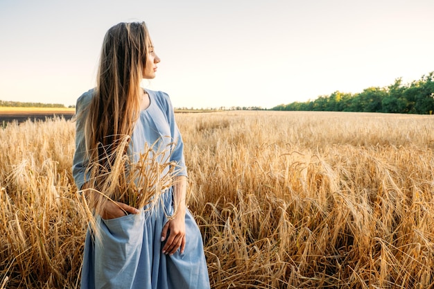 Ukrainische junge Frau, die während des sonnigen Tages Weizenernte auf dem Feld hält, gesichtsloses Porträt von