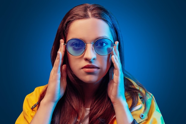 Ukrainische junge Frau in gelbem Regenmantel und runder Olor-Brille auf blauem Hintergrund