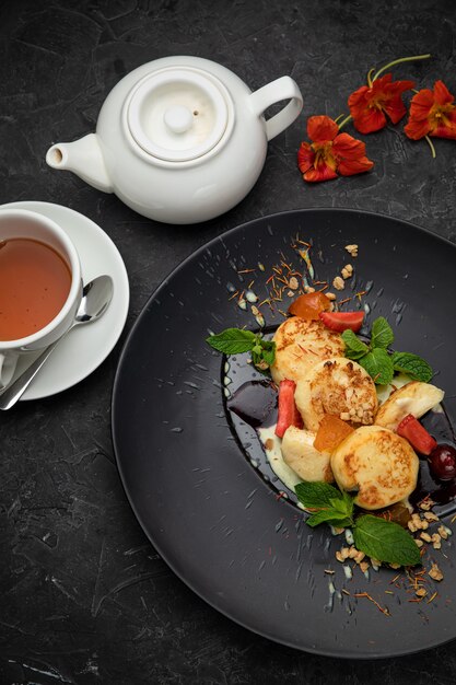 Ukrainische Käsekuchen mit Saucen, Beeren und Minze in einem dunklen Teller