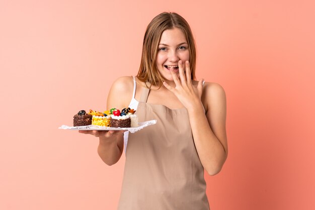 Ukrainischer Gebäckkoch, der Muffins hält, die auf rosa Raum mit überraschendem Gesichtsausdruck isoliert werden