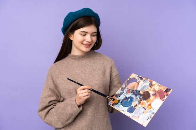 Ukrainisches junges Künstlermädchen, das eine Palette über purpurroter Wand mit glücklichem Ausdruck hält