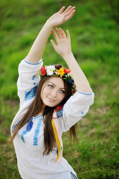 Ukrainisches Mädchen in einem Hemd und einem Blumenkranz auf dem Kopf, der Ihre Hände hochzieht