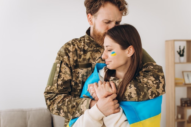 Ukrainisches Paar Militärmann in Uniform umarmt und wickelt seine Frau in die ukrainische Flagge Das Konzept des Patriotismus