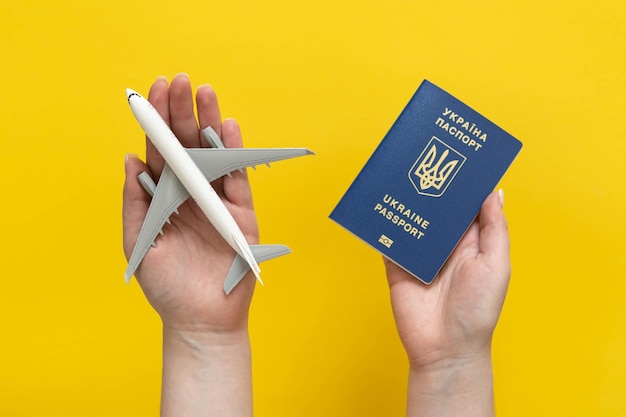 Ukrainisches Pass- und Flugzeugmodell in weiblichen Händen auf gelbem Hintergrund