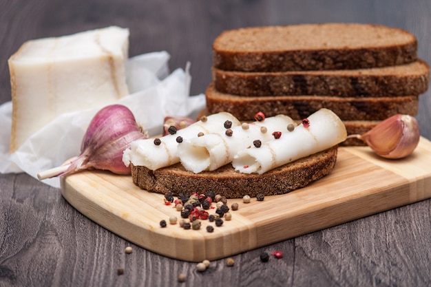 Ukrainisches traditionelles Essen - Salo. Geschnittener Speck mit dunklem Brot, Knoblauch, Pfeffer auf hölzernem Brett