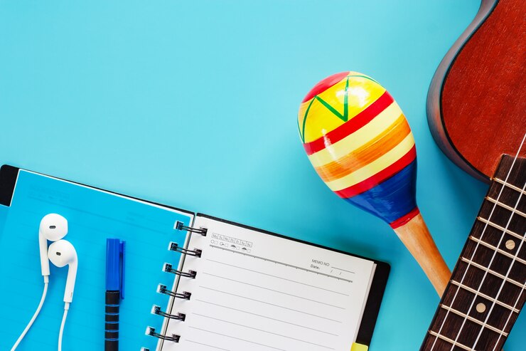 Foto ukulele com maracas, abriu o caderno espiral, caneta e fones de ouvido no fundo azul