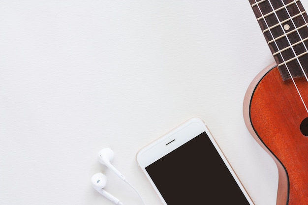 Ukulele com smartphone e fones de ouvido no fundo branco